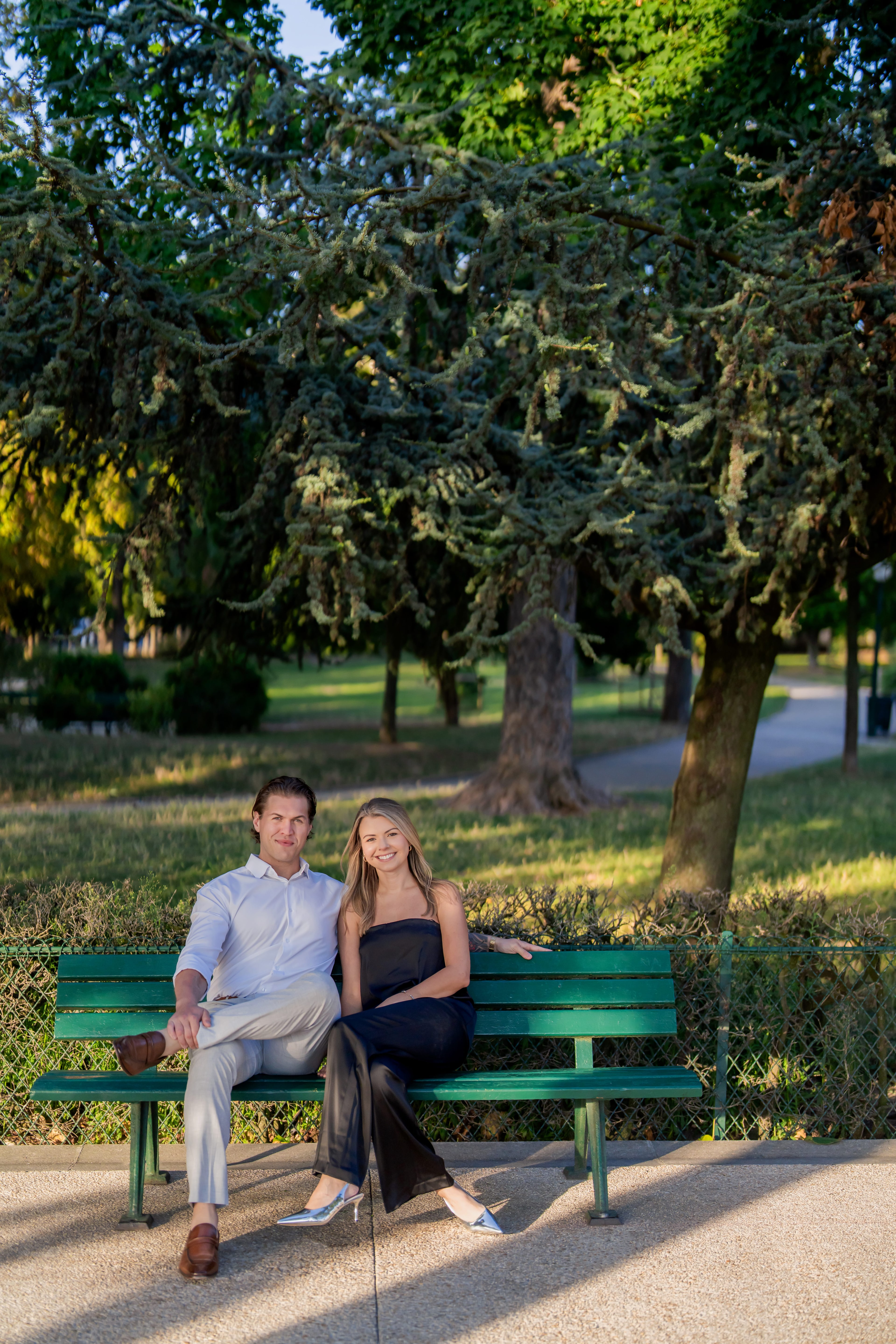 Austin and Andrea seated on a green park bench beneath a tree
